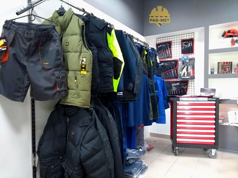 Ekspozycja odzieży roboczej w sklepie: szorty robocze z kieszeniami, kamizelka ocieplana khaki, kurtki puchowe i robocze, narzędzia GTools na ścianie i w wózku narzędziowym z czerwonymi szufladami,...