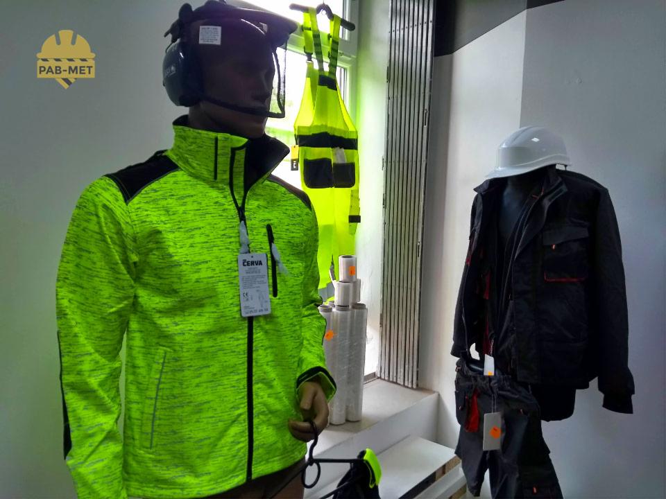 Ekspozycja odzieży roboczej: manekin w neonowo-zielonej kurtce z czarnymi wstawkami, kask ochronny z osłoną twarzy i słuchawkami, obok kombinezon ostrzegawczy na wieszaku i zestaw czarnej kurtki...