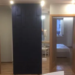 Wnętrze mieszkania po remoncie: widok na pokój przez otwarte drzwi, z fragmentem ściany z cegły dekoracyjnej po prawej, oraz czarnym panelem ściennym po lewej stronie.