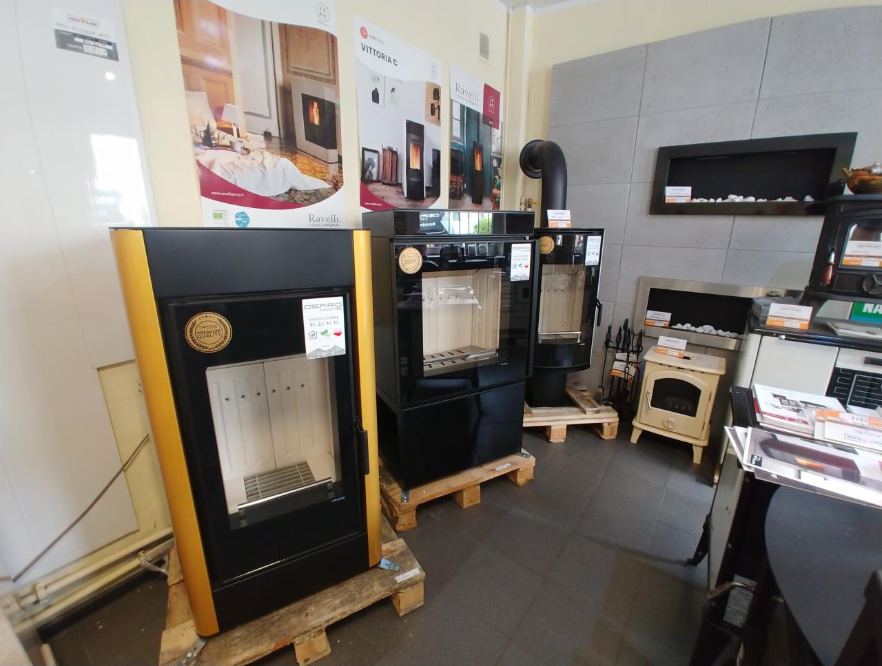 Ekspozycja w salonie: nowoczesne piece wolnostojące o różnych konstrukcjach, w tym model z obudową w kolorze czarnym ze złotymi akcentami, oraz wkłady do zabudowy z dekoracyjnymi kamieniami.