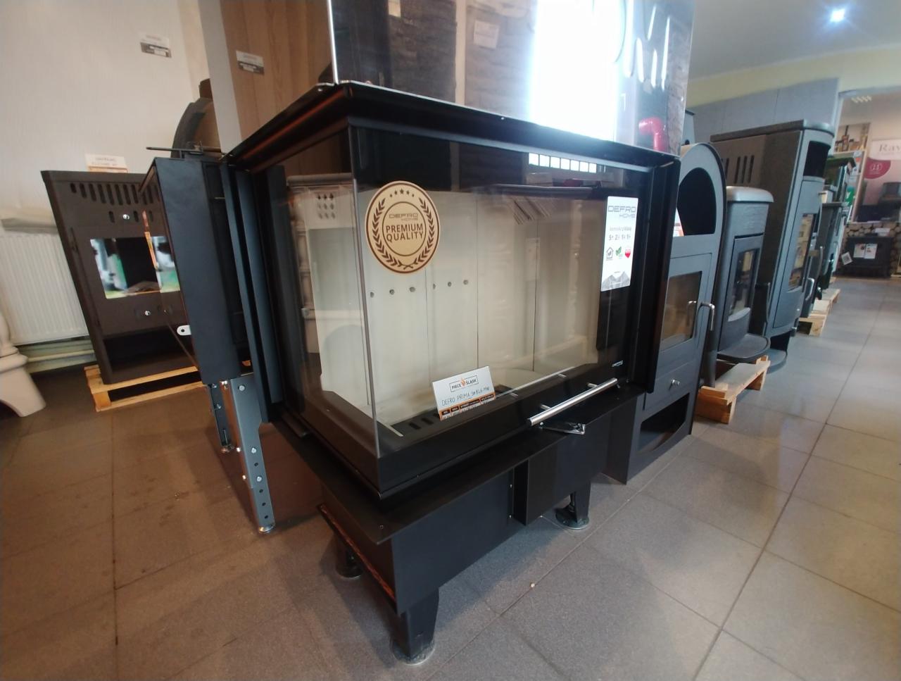 Wystawa w salonie: nowoczesny wkład kominkowy z szybą, oznaczony naklejką 'Premium Quality', na tle innych modeli pieców i wkładów.