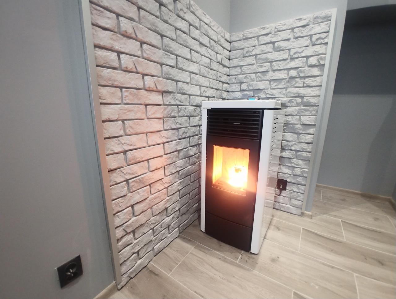Nowoczesny piec wolnostojący na pellet w Siemianowicach Śląskich, z płomieniem widocznym za szybą, ustawiony na podłodze z płytek imitujących drewno, z dekoracyjną ścianą z cegły w tle.
