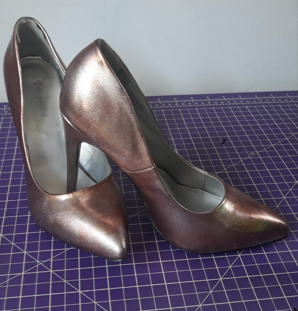 Para damskich szpilek w kolorze różowego złota, ustawionych na fioletowej macie do cięcia, z widocznym logo 'Via Giulia' na wewnętrznej stronie buta po lewej.