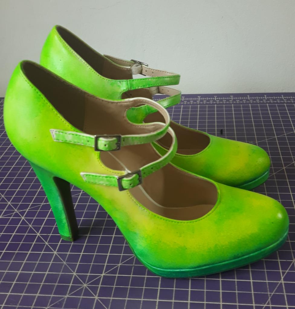 Para damskich butów na wysokim obcasie w odcieniach jaskrawej zieleni, z podwójnymi paskami zapinanymi na sprzączki, leżących na fioletowej macie do cięcia.