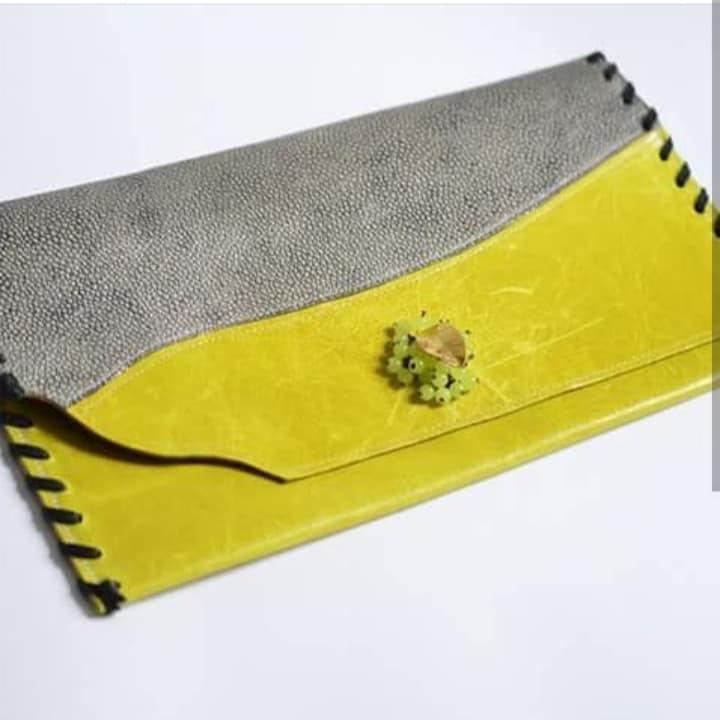 Żółto-szara skórzana kopertówka z ozdobną aplikacją z koralików, z czarnymi przeszyciami na krawędziach, leżąca na białym tle.