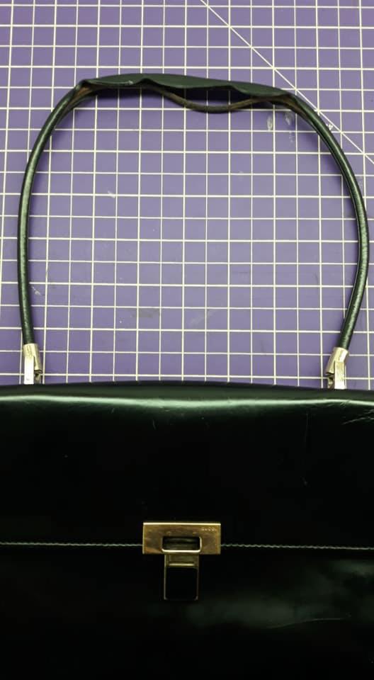 Czarna skórzana torebka z metalowym zapięciem i uchwytem na fioletowej macie do cięcia.