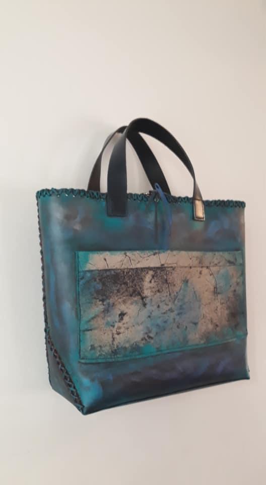 Turkusowa, ręcznie szyta torba skórzana z abstrakcyjnym wzorem na kieszeni, wykończona plecionką na krawędziach.