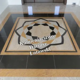 Wzorzysta posadzka kamienna z centralnym motywem rozety w odcieniach beżu, czerni i brązu, otoczona geometrycznym obramowaniem, widok z góry.