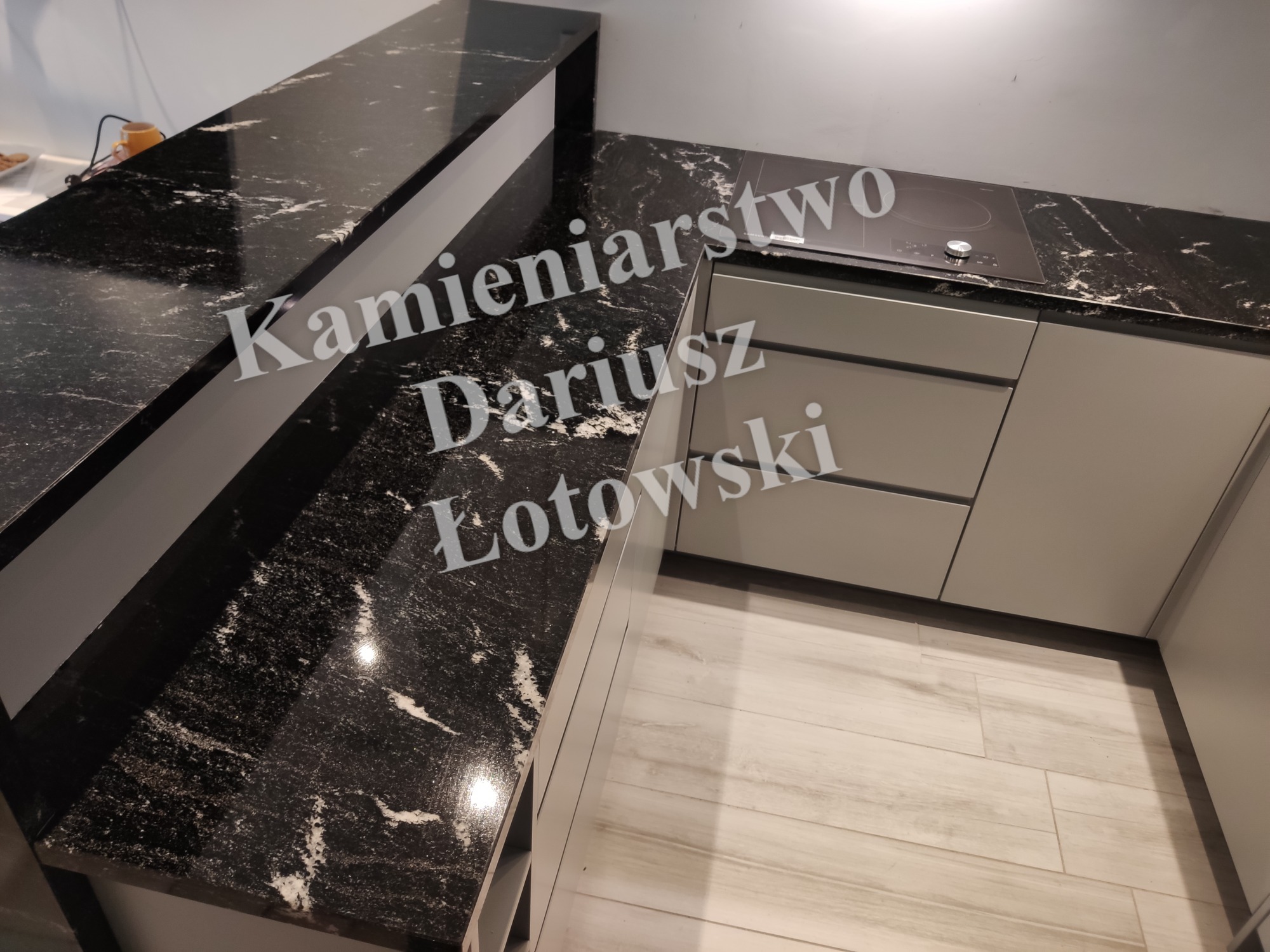 Czarny blat z białymi żyłkami, zamontowany w nowoczesnej kuchni z szarymi szafkami i płytą indukcyjną.