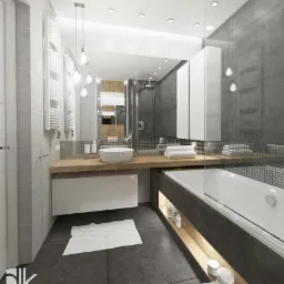 Nowoczesna łazienka z szarymi płytkami, drewnianym blatem pod umywalką i podświetlaną wnęką przy wannie, uzupełniona o białe akcenty i minimalistyczne oświetlenie.