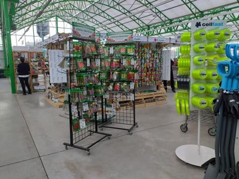 Wnętrze sklepu ogrodniczego z regałami wypełnionymi opakowaniami nasion i narzędziami ogrodniczymi, widoczne osoby w tle.