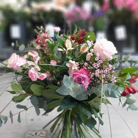 Delikatny bukiet z różowych róż, alstromerii i eukaliptusa, z drobnymi różowymi kwiatami wypełniającymi przestrzeń, na rozmytym tle innych kwiatów.