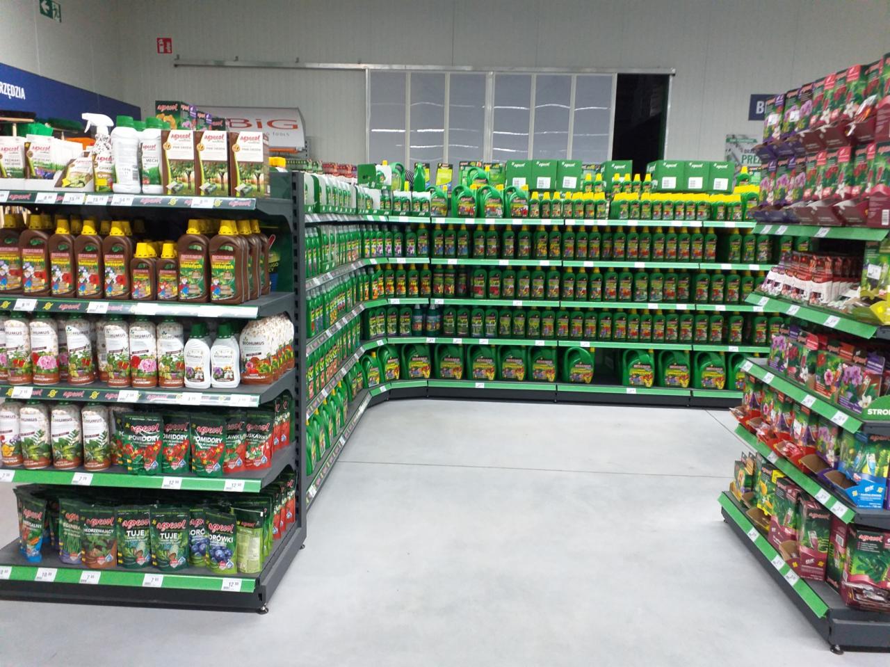 Półki sklepowe wypełnione różnorodnymi opakowaniami nawozów i środków do pielęgnacji roślin, ustawione w rzędach i kolumnach, tworzące perspektywę w głąb sklepu.