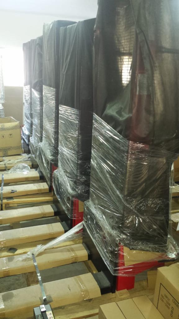 Rząd zapakowanych w folię i przykrytych czarną folią wózków na drewnianych paletach w magazynie. Wózki mają czerwone elementy konstrukcyjne.