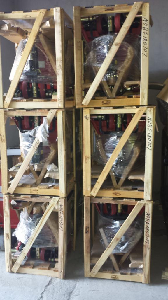 Elektryczne wózki paletowe zapakowane w drewniane skrzynie transportowe, zabezpieczone folią, ustawione jeden na drugim.