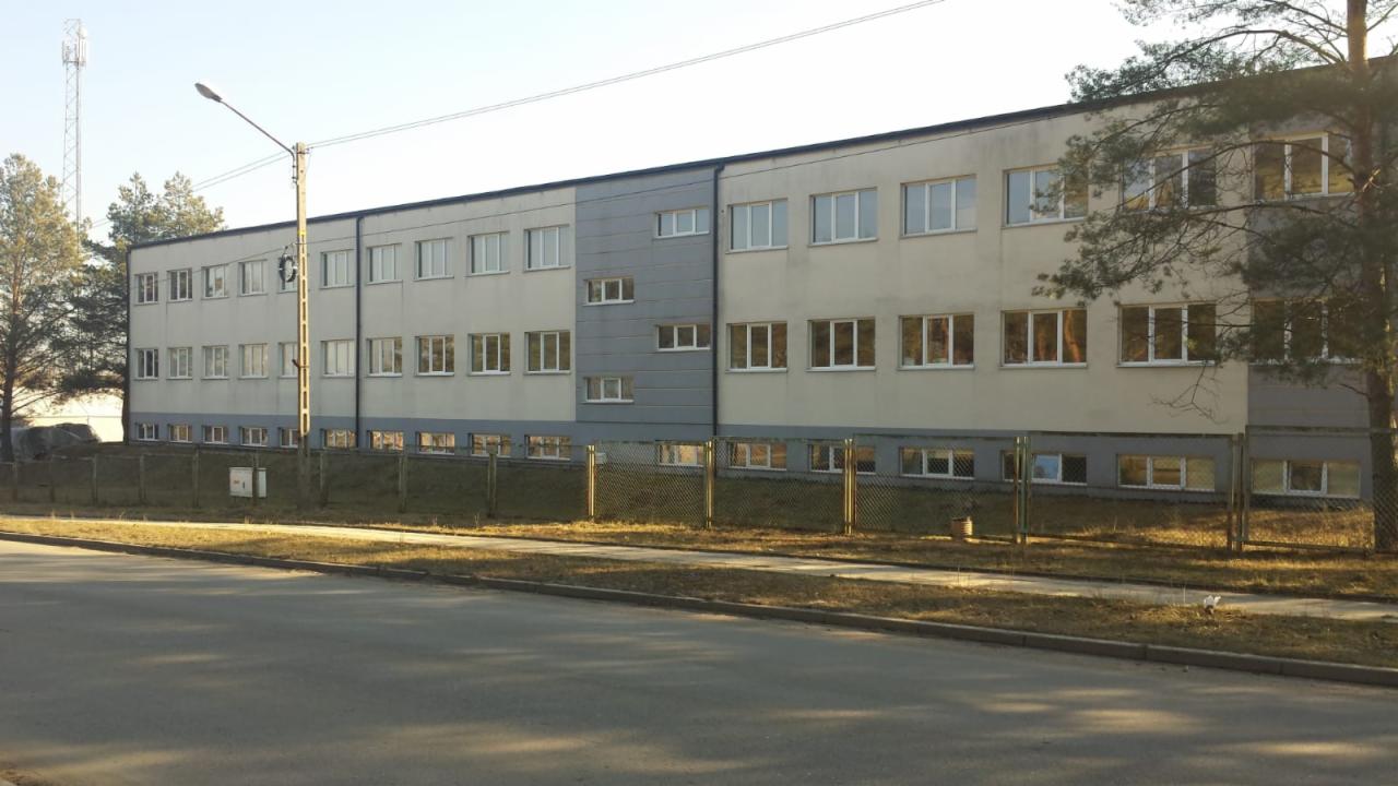 Dwukondygnacyjny budynek biurowy z licznymi oknami, widoczny z poziomu ulicy, ogrodzony siatką.