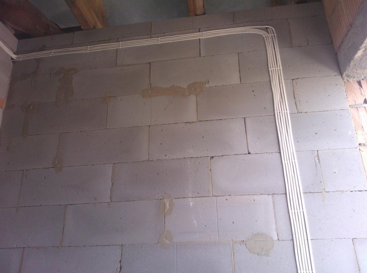 Świeżo poprowadzone, białe przewody elektryczne ułożone wzdłuż szarej ściany z bloczków betonu komórkowego w trakcie budowy w Krakowie. Widoczne ślady po zaprawie murarskiej.