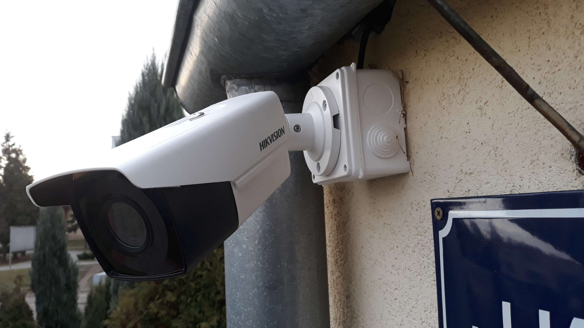 Biała kamera Hikvision zamontowana na elewacji budynku, widoczna puszka instalacyjna i fragment tabliczki z nazwą ulicy.