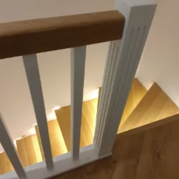 Widok z góry na drewniane schody z białymi balustradami i drewnianym poręczą, oświetlone od spodu, z podłogą ułożoną w jodełkę.