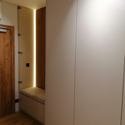 LESZEK BRZOZOWSKI - Minimalistyczna zabudowa przedpokoju w Poznaniu z dużą, jasną szafą, wnęką z drewnianymi lamelami podświetloną ledami i siedziskiem z tapicerowanym blatem.