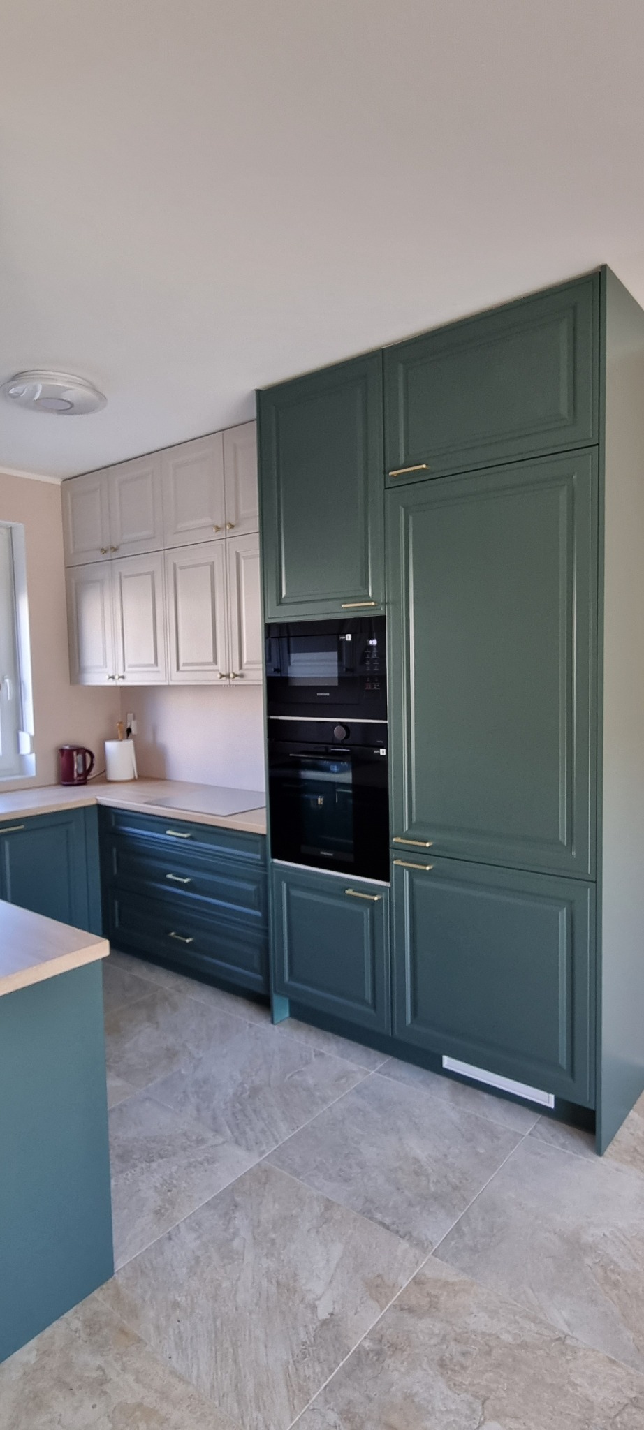 Nowoczesna kuchnia z elementami w odcieniach butelkowej zieleni i szarości, z zabudowaną czarną kuchenką mikrofalową i piekarnikiem, wykończona złotymi uchwytami.