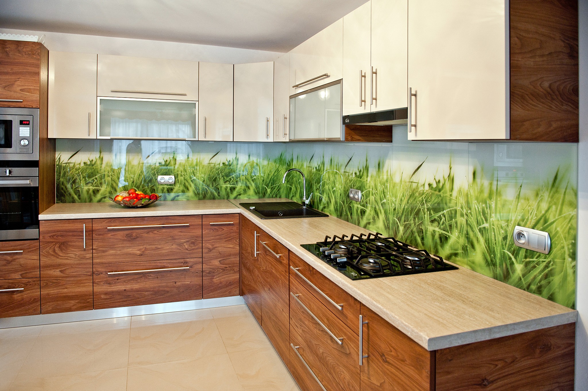 Nowoczesna kuchnia z drewnianymi szafkami i szklanym panelem ściennym z motywem trawy, z czarnym zlewem i płytą gazową. Jasne, przestronne wnętrze.