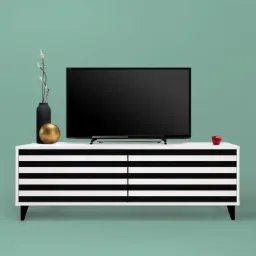 Biała szafka RTV z czarnymi poziomymi pasami, na niej czarny telewizor, czarny wazon z gałązkami, złota kula i czerwone jabłko na tle miętowej ściany.