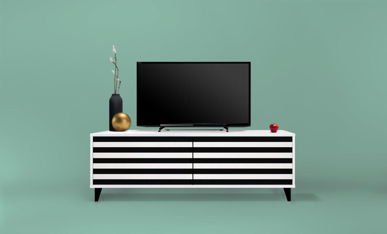 Biała szafka RTV z czarnymi poziomymi pasami, na niej czarny telewizor, czarny wazon z gałązkami, złota kula i czerwone jabłko na tle miętowej ściany.
