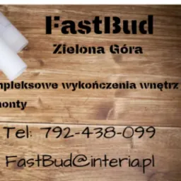 Wizytówka firmy FastBud z Zielonej Góry na drewnianym tle, oferującej kompleksowe wykończenia wnętrz i remonty, z numerem telefonu i adresem email, obok zwinięte plany architektoniczne.