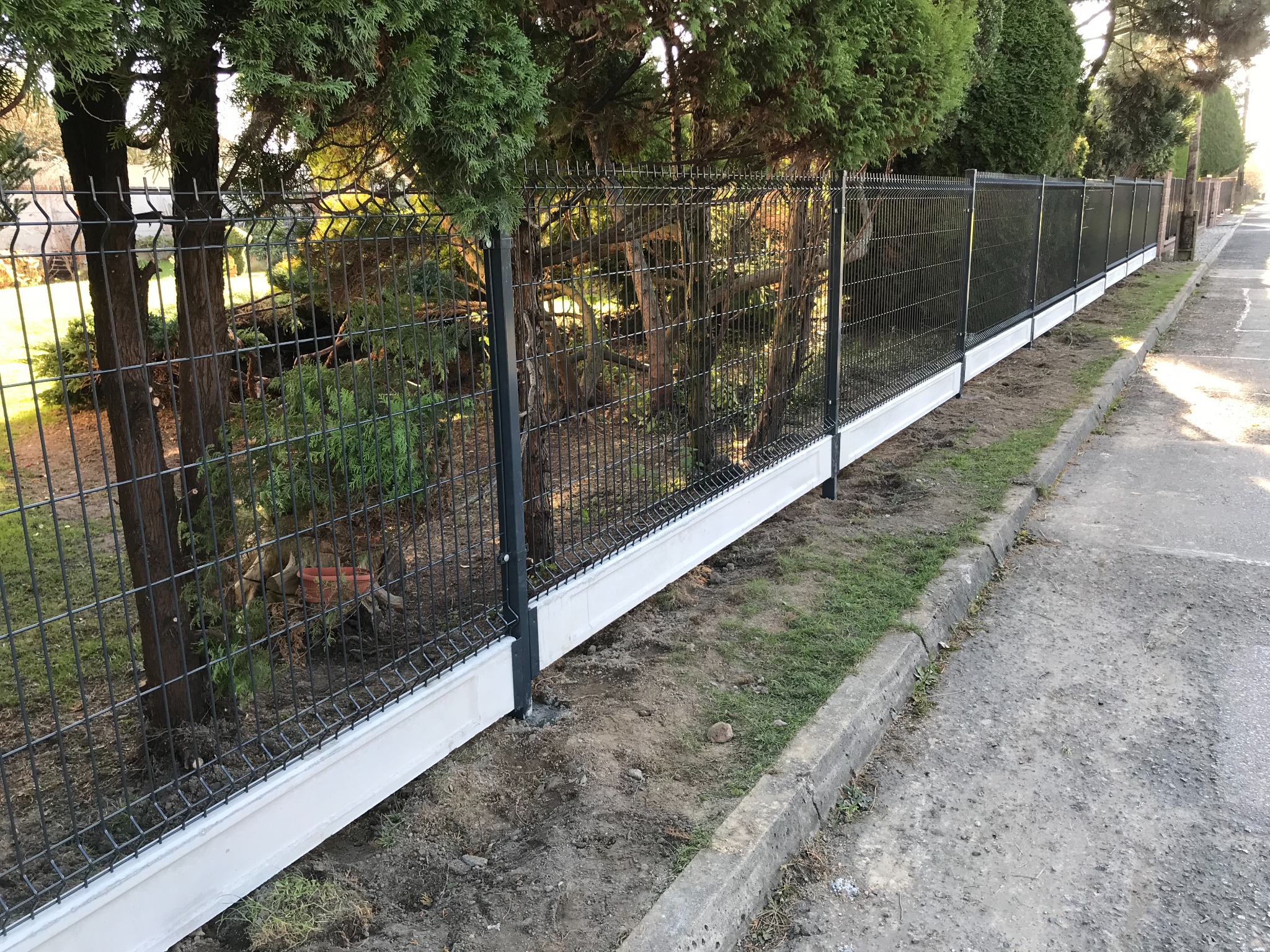 Nowoczesne ogrodzenie panelowe z podmurówką betonową, widok z zewnątrz posesji, zieleń w tle.