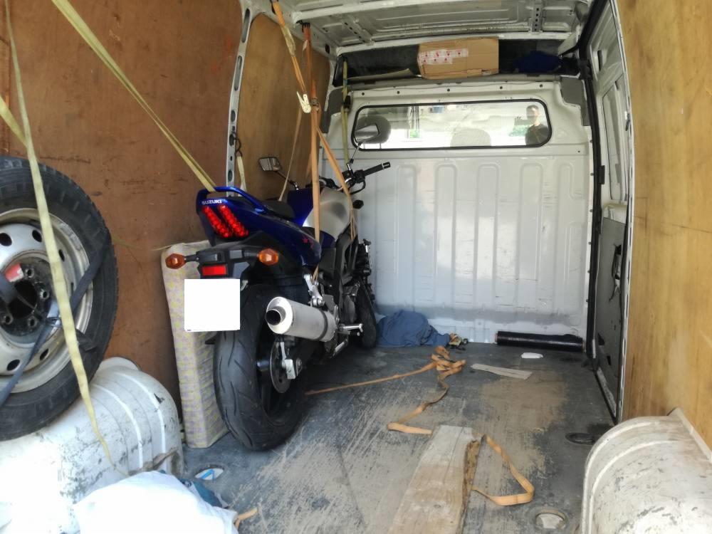 Wnętrze furgonetki z zabezpieczonym motocyklem Suzuki, dodatkowym kołem i elementami wyposażenia, przygotowanymi do transportu.