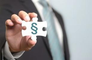 Mężczyzna w garniturze trzyma element układanki z symbolem paragrafu. Ujęcie z bliska, rozmyte tło.