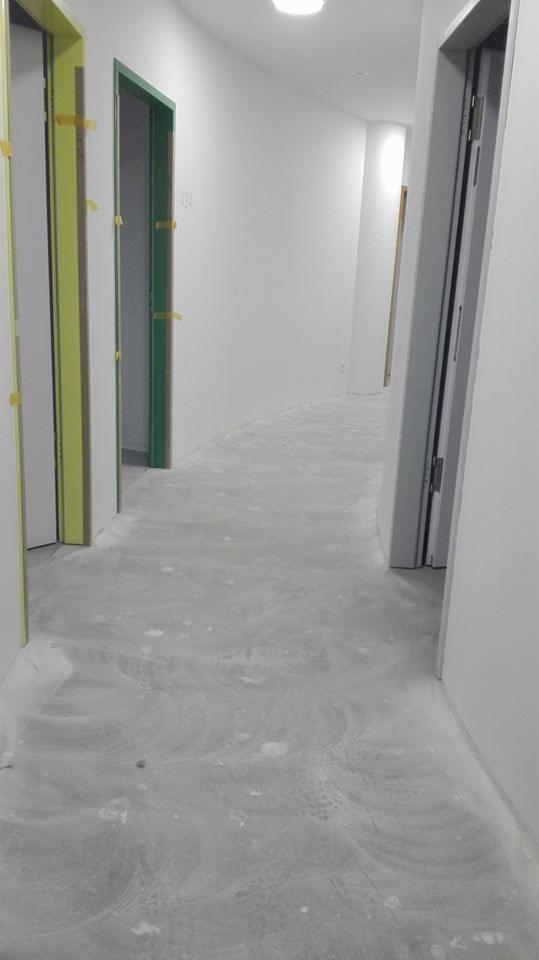 Korytarz w trakcie remontu z widocznymi śladami gładzi na podłodze, drzwi oklejone taśmą malarską w różnych kolorach.