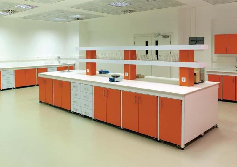 Nowoczesne meble laboratoryjne w odcieniach bieli i pomarańczy, z blatami z białego konglomeratu, szafkami z gładkimi frontami i widocznymi naczyniami laboratoryjnymi na półkach w tle, oświetlenie...