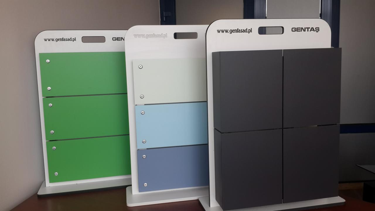 Ekspozycja próbek elewacyjnych Gentaş w kolorach zieleni, błękitu i szarości, prezentowanych na białych stojakach z widocznym adresem www.genfasad.pl.