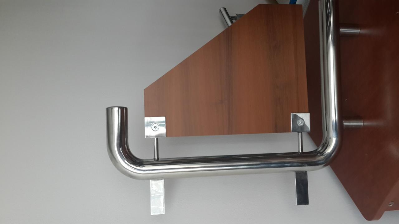 Fragment szafy wnękowej z elementami metalowymi, widoczne mocowania i rurki ze stali nierdzewnej, drewniana płyta w kolorze orzechowym, minimalistyczny design.