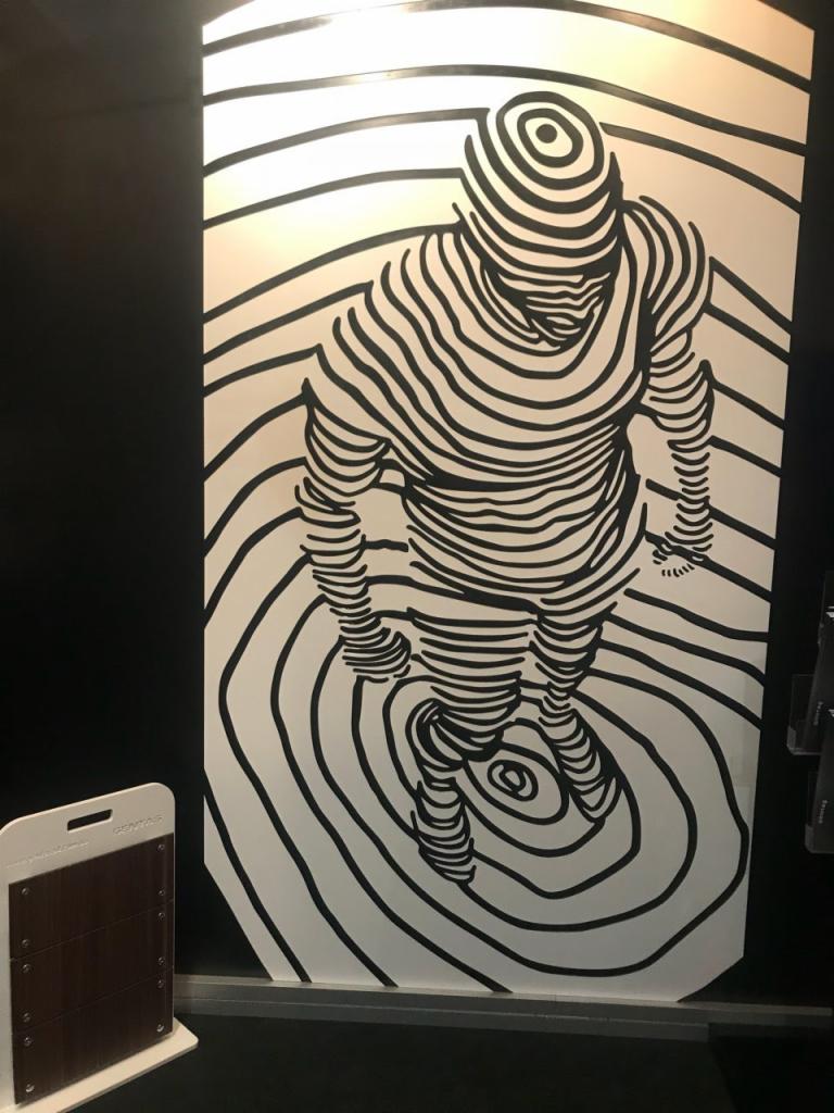 Ilustracja przedstawiająca postać ludzką utworzoną z czarnych koncentrycznych linii na białym tle, przypominająca efekt optyczny lub wizualizację 3D, obok próbnik materiału wykończeniowego.