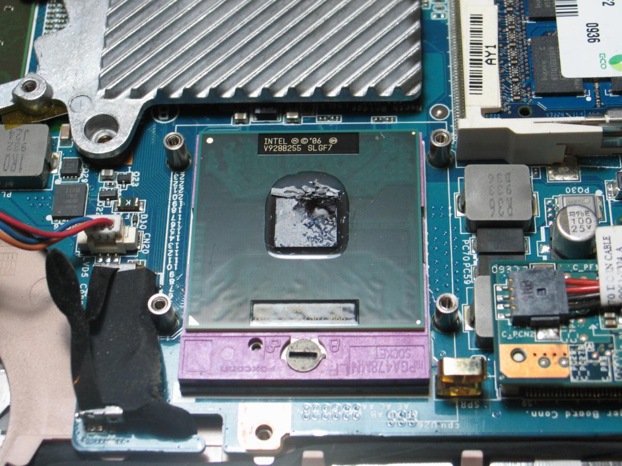 Otwarty socket procesora Intel z widoczną pastą termoprzewodzącą na procesorze, otoczony elementami płyty głównej laptopa.