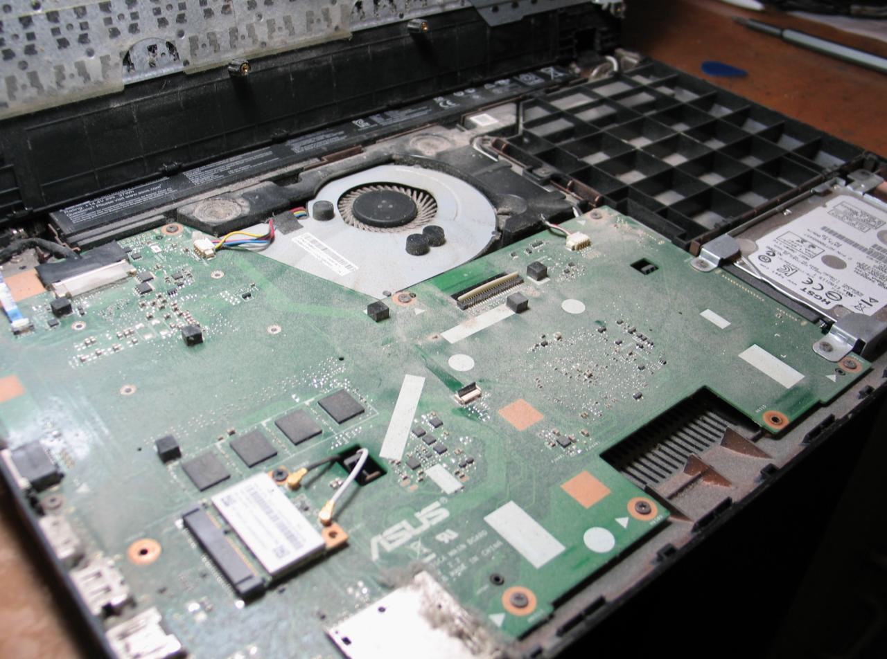 Otwarty laptop ASUS z widoczną zakurzoną płytą główną, wentylatorem i dyskiem twardym podczas serwisu.