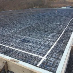 Siatka zbrojeniowa ułożona na folii, przygotowana do wylania fundamentów, widoczne szalunki drewniane.