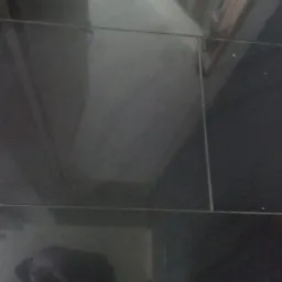 Błyszcząca, czarna podłoga z płytek, widoczne odbicia i fugi, niedoskonałe oświetlenie.