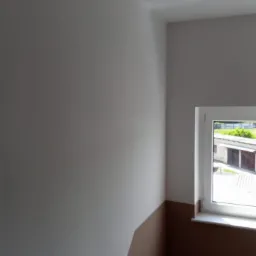 Świeżo pomalowane wnętrze z dwukolorową ścianą; górna część szara, dolna brązowa, widoczne okno z białymi ramami i widokiem na budynek gospodarczy.