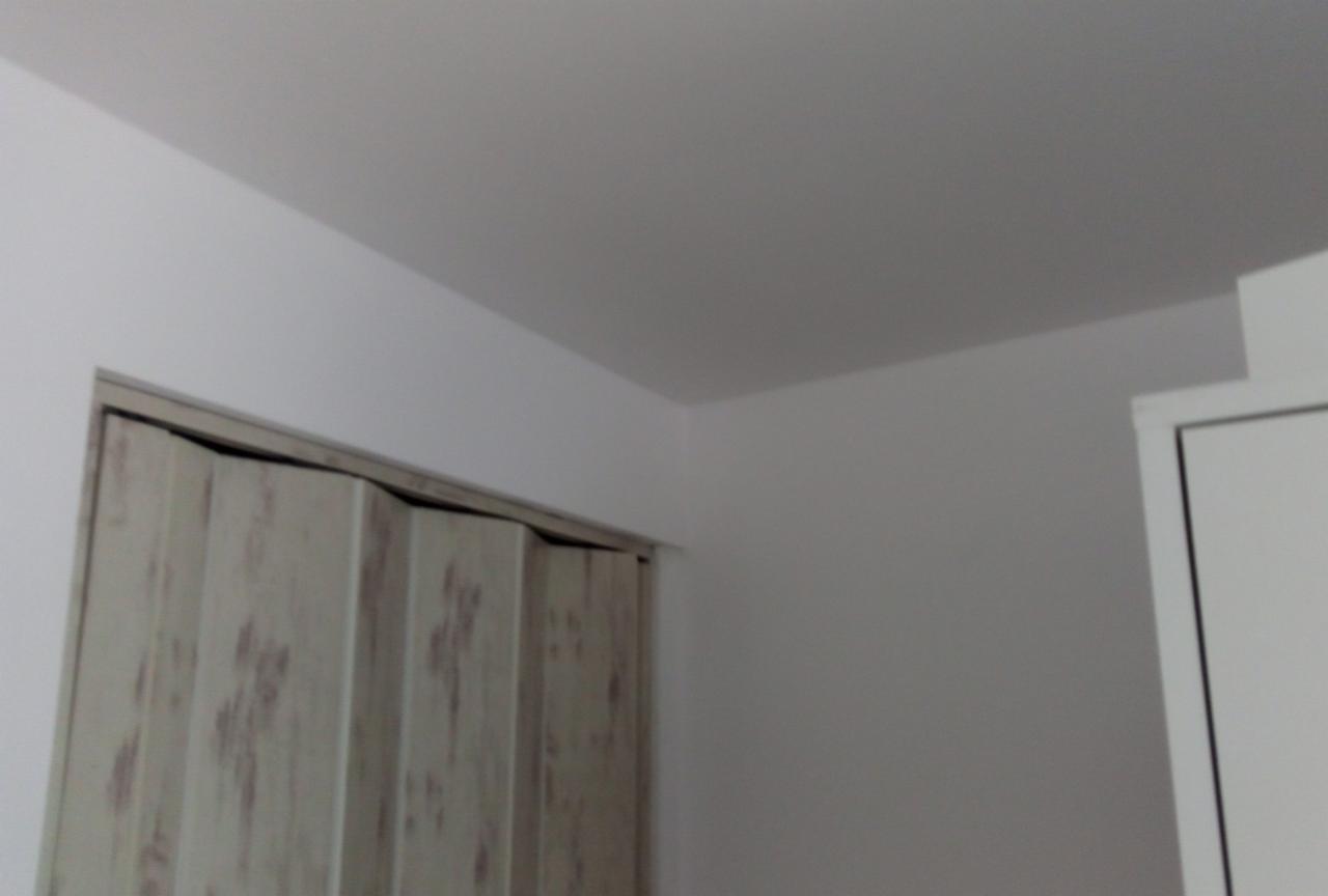 Fragment wnętrza z widocznym składanym, drewnopodobnym skrzydłem drzwiowym w ościeżnicy oraz świeżo pomalowaną ścianą na biało.