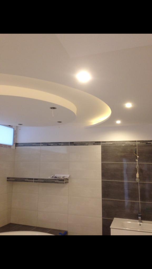 Wykończona łazienka z podwieszanym sufitem z oświetleniem punktowym, płytkami w odcieniach beżu i brązu, oraz elementami dekoracyjnymi w postaci czarnych pasków.