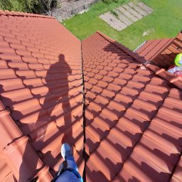 Michał - Czerwona dachówka karpiówka z widocznym pęknięciem na łączeniu połaci, cień osoby na dachu, w tle trawnik i grządki.