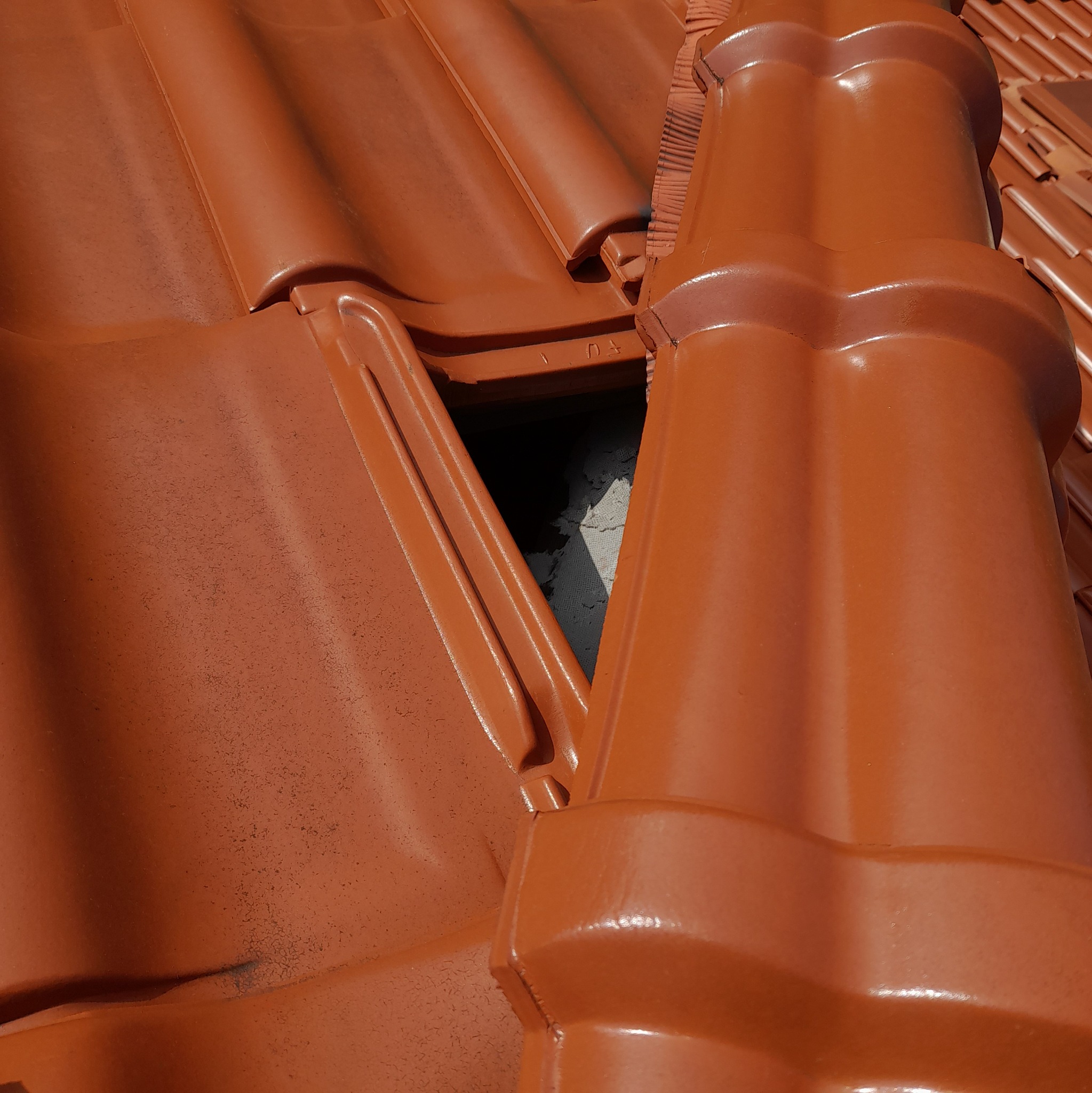 Brązowa dachówka ceramiczna z ubytkiem, ukazującym warstwę izolacyjną pod spodem, widoczne ślady użytkowania na powierzchni dachówek.