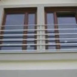 Nierdzewna balustrada okienna z poziomych rurek, zamontowana na elewacji budynku, widoczna z zewnątrz, z oknami z brązowymi ramami w tle.