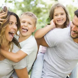 Radosna rodzina z dwójką dzieci na spacerze w parku, tata i mama dają dzieciom przejażdżkę na barana, wszyscy się śmieją i dobrze bawią.