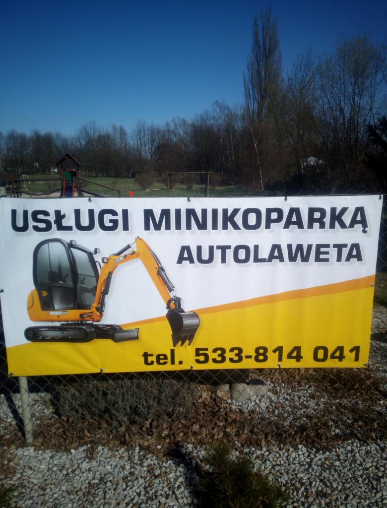 Baner reklamowy usług minikoparką i autolawetą z ilustracją koparki JCB 8008 CTS, zawieszony na ogrodzeniu z siatki.