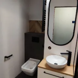 Nowoczesna łazienka w odcieniach bieli i czerni z umywalką nablatową, bidetem i kabiną prysznicową z deszczownicą.